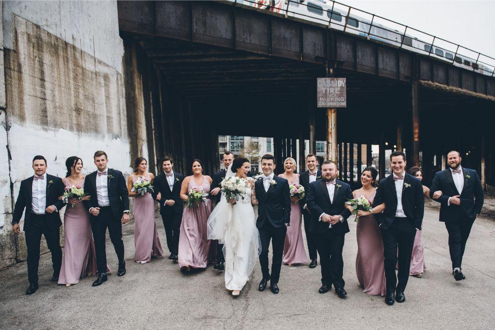 A group of bridesmaids and groomsmen standing together with the married couple, the bridesmaids are wearing Very Peri colored dresses.